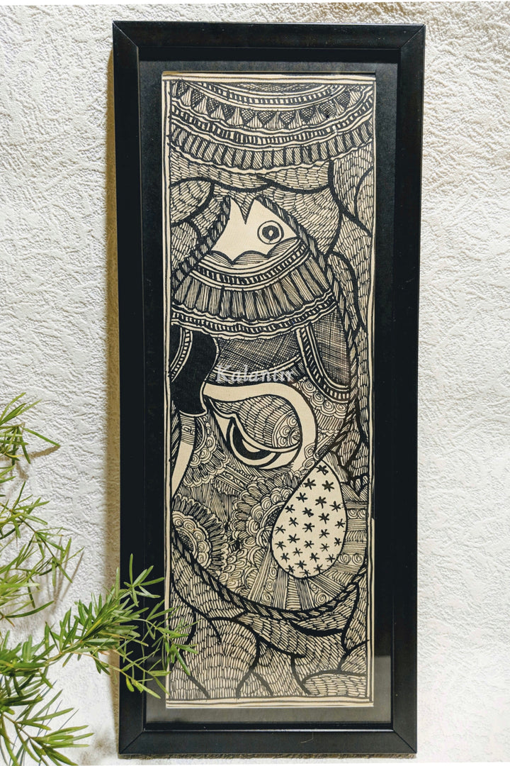 Framed Black and White Madhubani Painting of Ganesha within Fish Motif, kept against a wall and near a green plant.